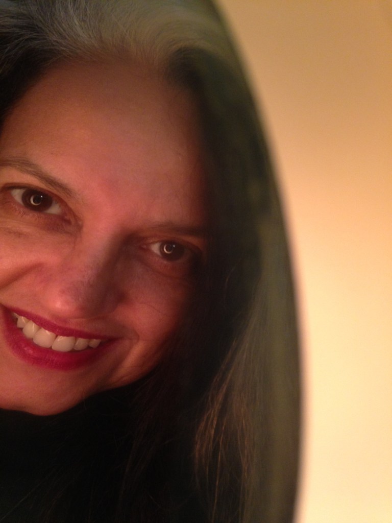 Rosto de Duaia Assumpção sorrindo sob uma luz quente. Boas vindas! Pode reparar, estamos em construção.