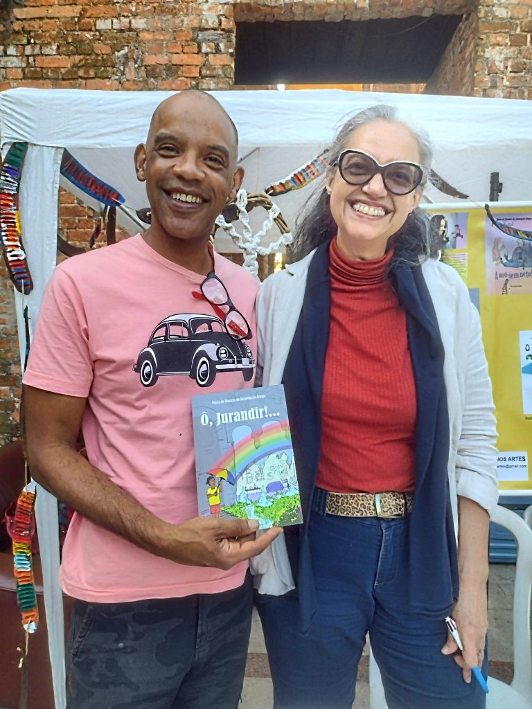 João Batista Pires com seu exemplar autografado de "Ô, Jurandir!...", abraçado à autora, Maria do Rosário (Duaia) de Assumpção Braga, na FLIST 2022, no Parque das Ruínas, Santa Teresa, RJ.